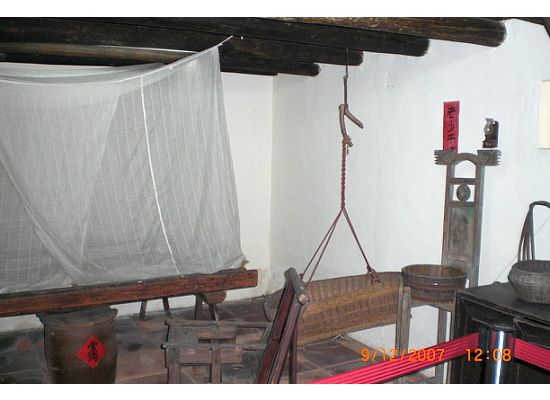 On the right hand side of the living room, there is a bedroom with drapes on top of the bed to block the bugs. Underneath the bed, there is a earthen container. It is for rice. On top of it, there is a piece of red paper with 2 Chinese characters that have the meaning "always full". It is the Chinese customs symbolizing abundance.