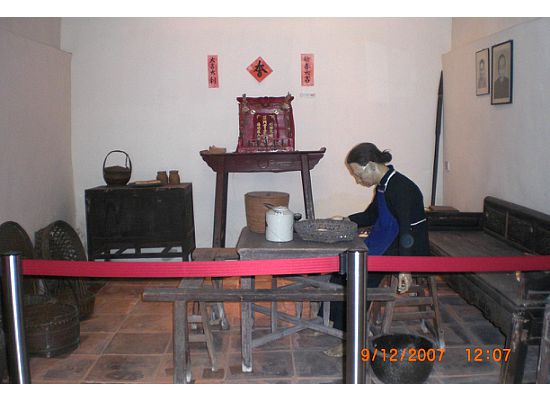 The lady in the living room is wearing an old Chinese country wife's outfit. In the middle of the wall, is the mantle where the house would worship their god and/or ancestors.